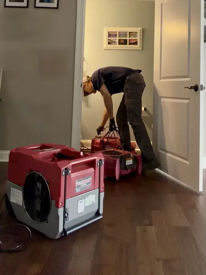 A technician setting up an LGR dehumidifier and air movers in a hallway