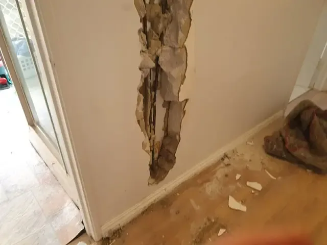 Drywall cut open at a doorway with debris on the floor after a leak