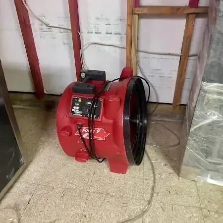 A red air mover drying a room with the lower wall opened and plastic sheeting hung after a leak