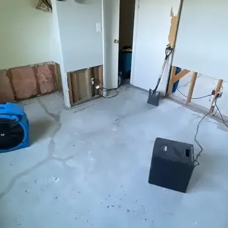 Air movers and a dehumidifier running in a room where the lower drywall was removed and the floor is bare
