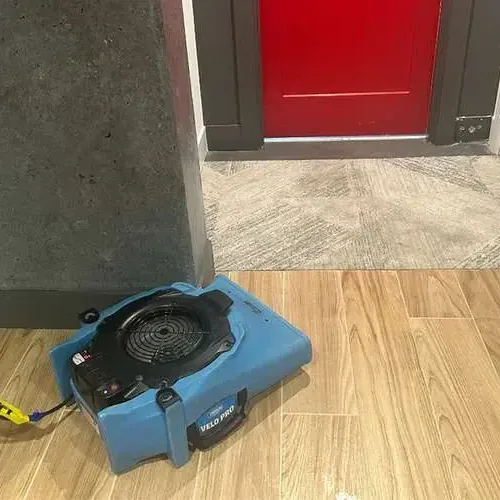 An air mover drying a wood-look tile floor beside an open doorway during a water damage dry-out
