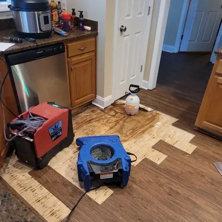 Flooring cut back in front of a dishwasher with drying equipment running in the kitchen