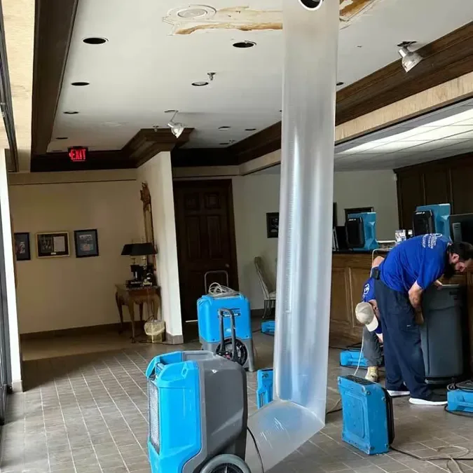 Dehumidifiers and a plastic air duct drying a commercial lobby with a stained ceiling