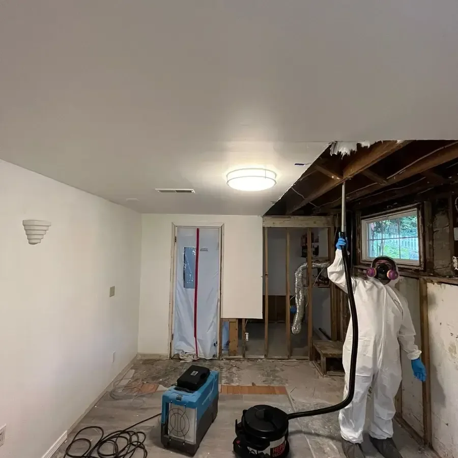 A technician in a protective suit and respirator working inside containment in a gutted room