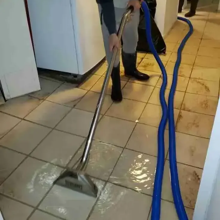An extraction wand drawing standing water off a tile floor inside a home